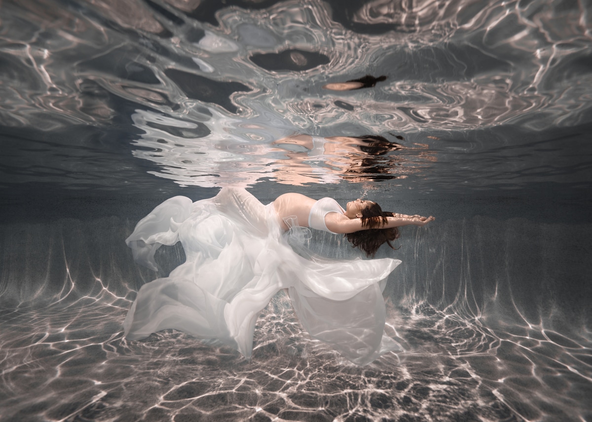 Pregnancy portrait underwater, maternity, woman floating on her back, wearing white flowing dress