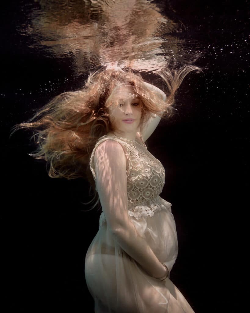 Underwater Maternity Fine Art Portrait Of A Pregnant Lady Wearing Lace And Chiffon Dress, With Flowing Red-blonde Hair, Black Background.