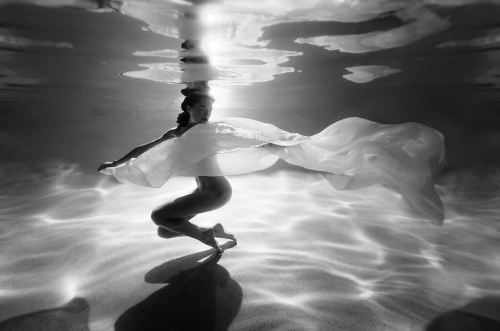 Artistic nude underwater portrait of woman dancing and floating underwater at night by moonlight, with a white floaty fabric, photographed on the Sunshine Coast, Queensland, Australia