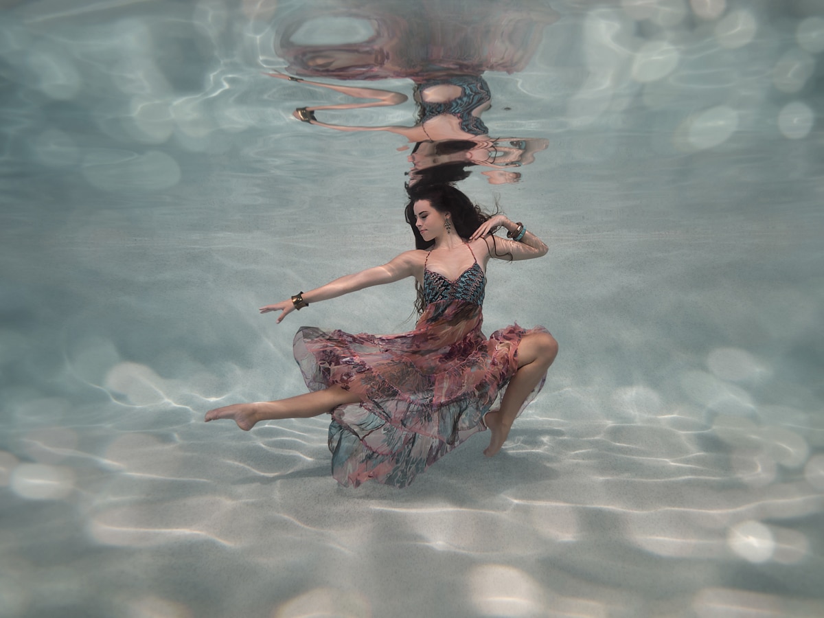 Woman ballet dancing underwater in a swimming pool, with chunky jewellery and boho gypsy dress; Sunshine Coast, Australia