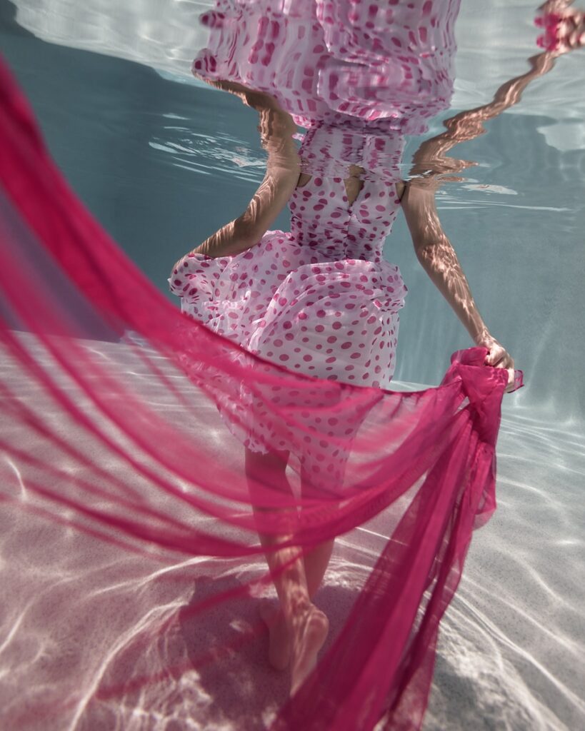 Underwater photo of a woman in a pink polka-dot dress, floating fabric, walking away