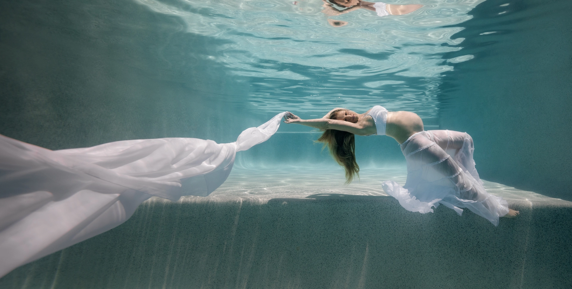 Underwater Maternity Portrait with Flowing White Fabric Underwater maternity portrait of a pregnant lady in a large swimming pool, wearing flowing white skirt and draping a long white chiffon scarf