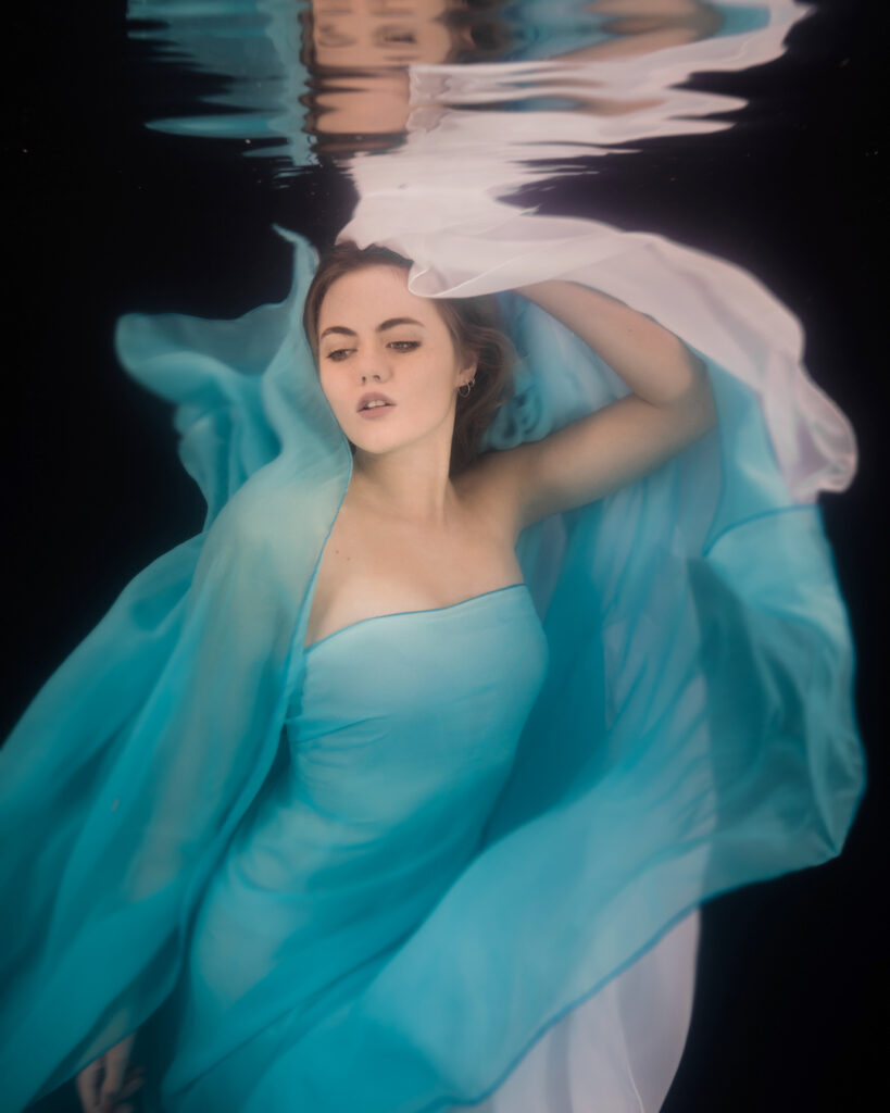 woman with chiffon floaty blue and white dress underwater with black background