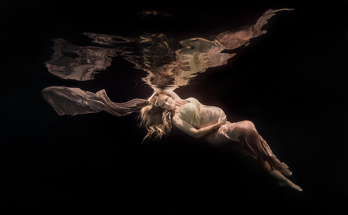 pregnant woman underwater wearing a gold dress and with long blonde hair
