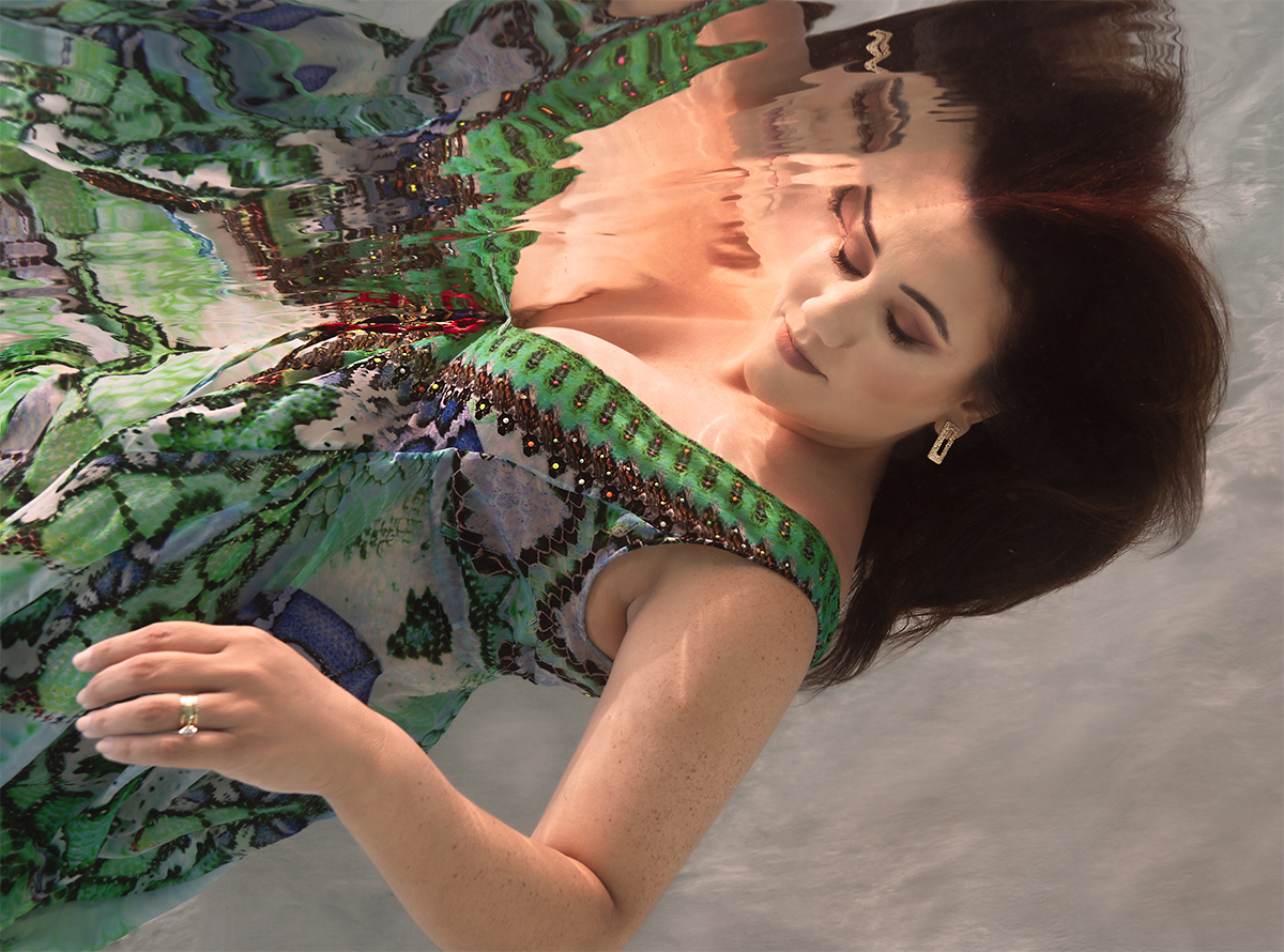 dark haired woman in beautifyl green patterened dress floating underwater