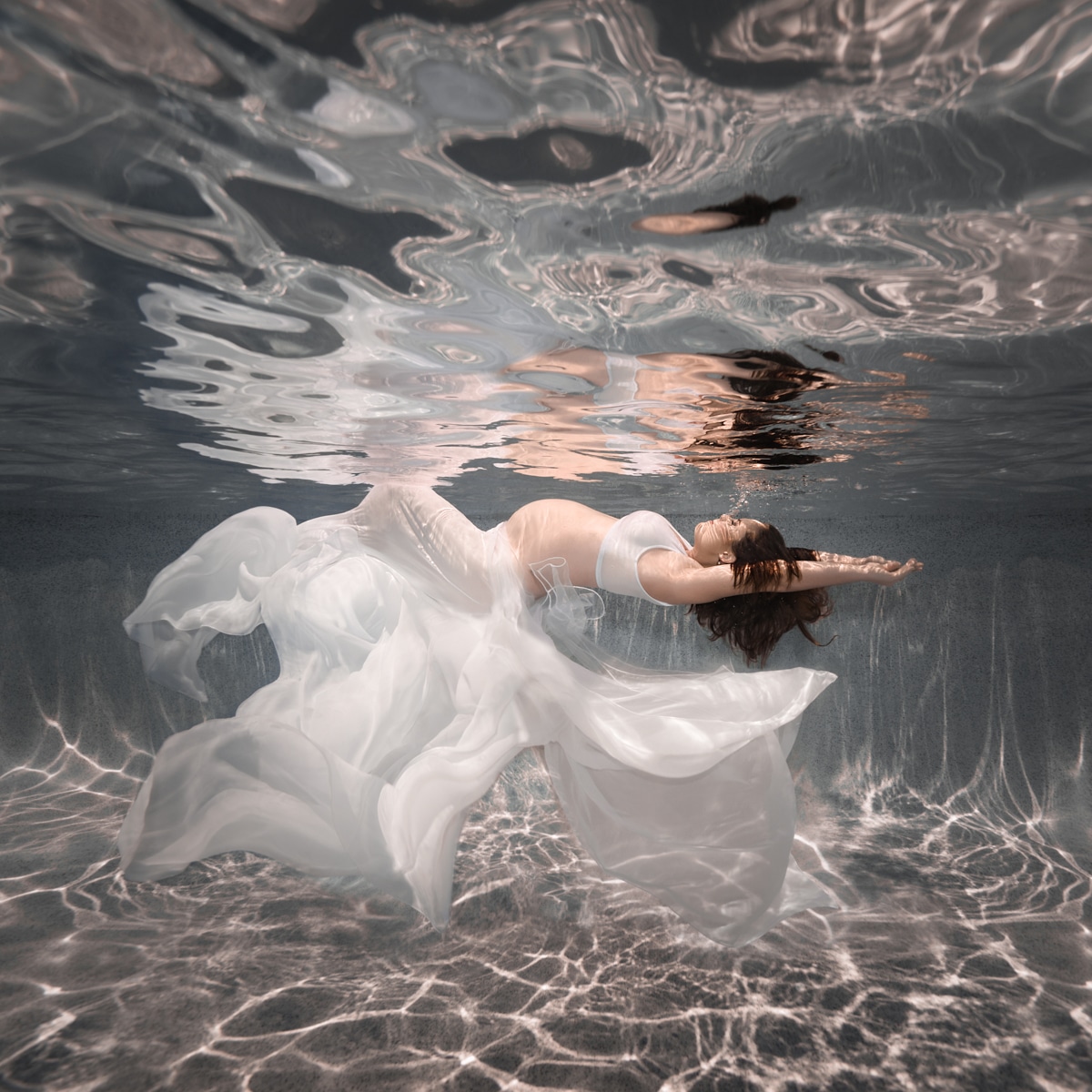 pregnant woman underwater wearing white skirt