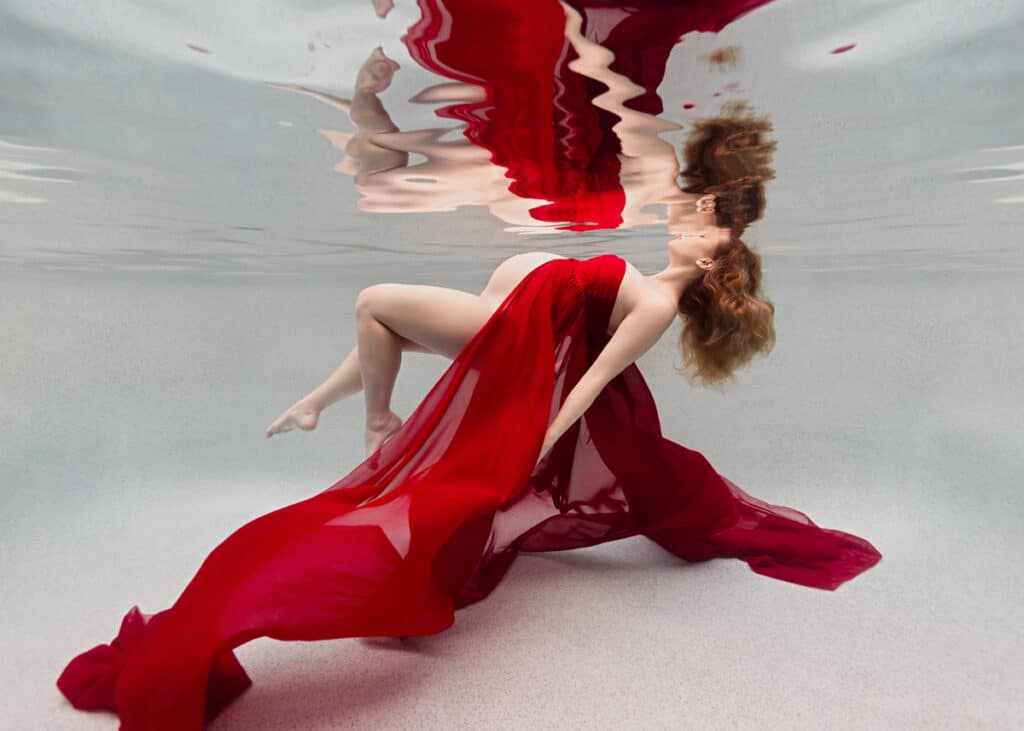 pregnant woman with long blonde hair wearing a flowing red gown underwater