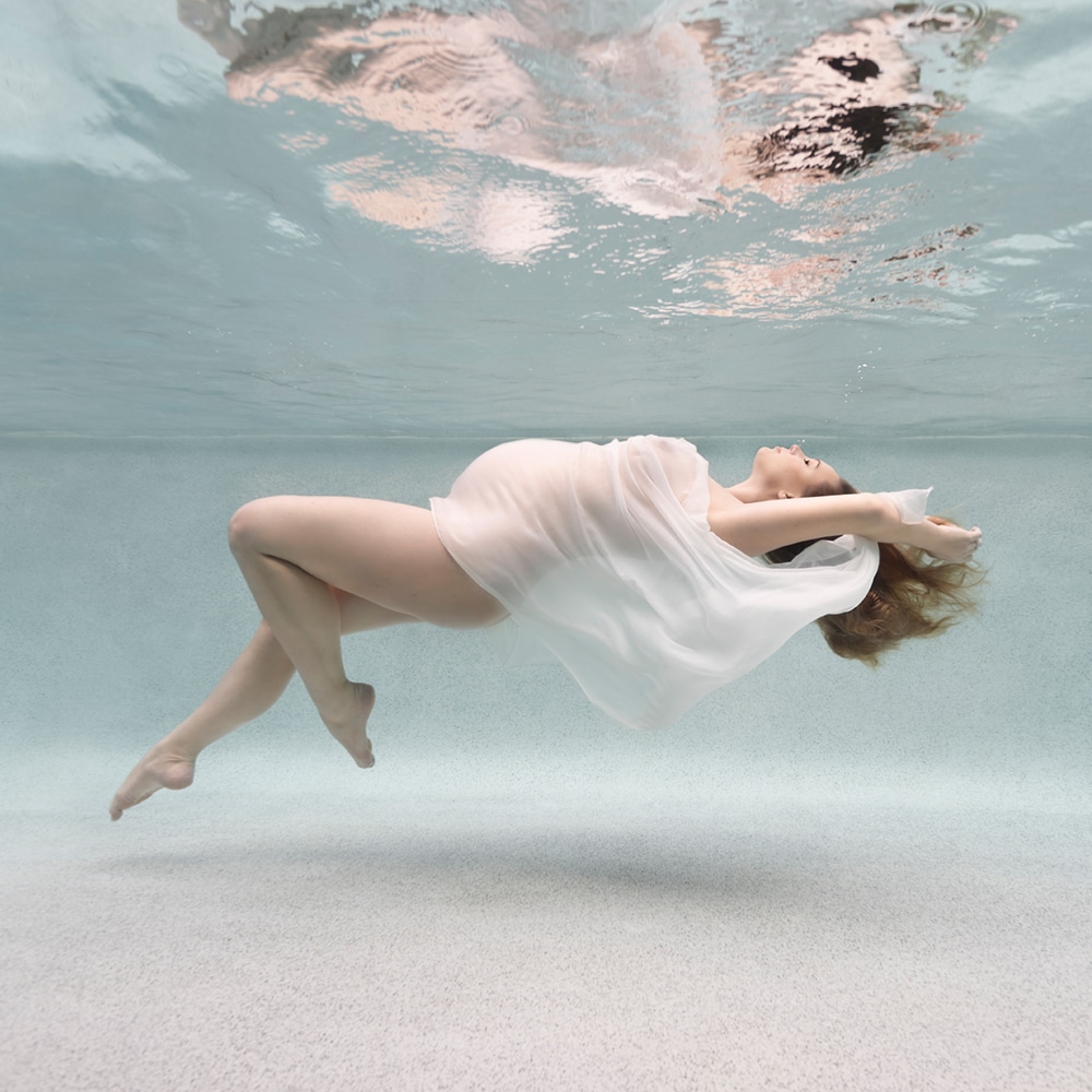 pregnanat woman floating underwater, draped in a white fabric