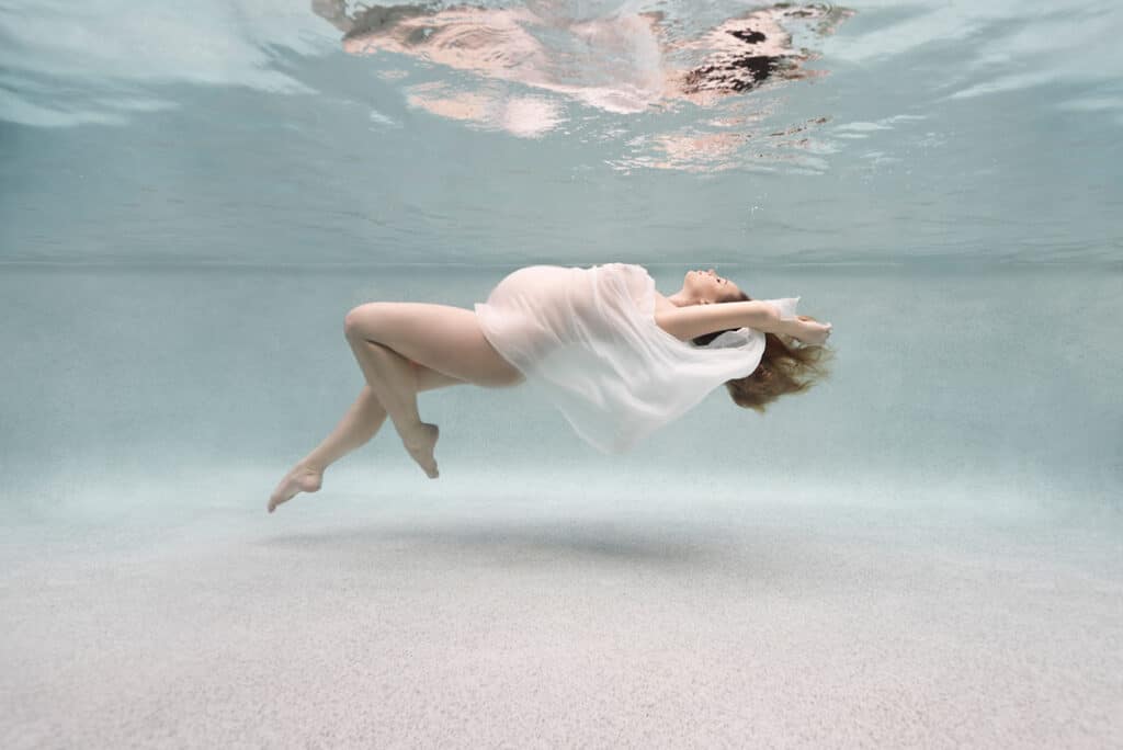 pregnancy woman floating underwater, her belly draped with a sheet white cloth