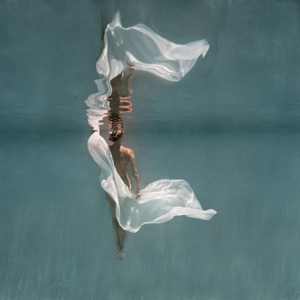 nude woman underwater covered by a white cloth, facing away