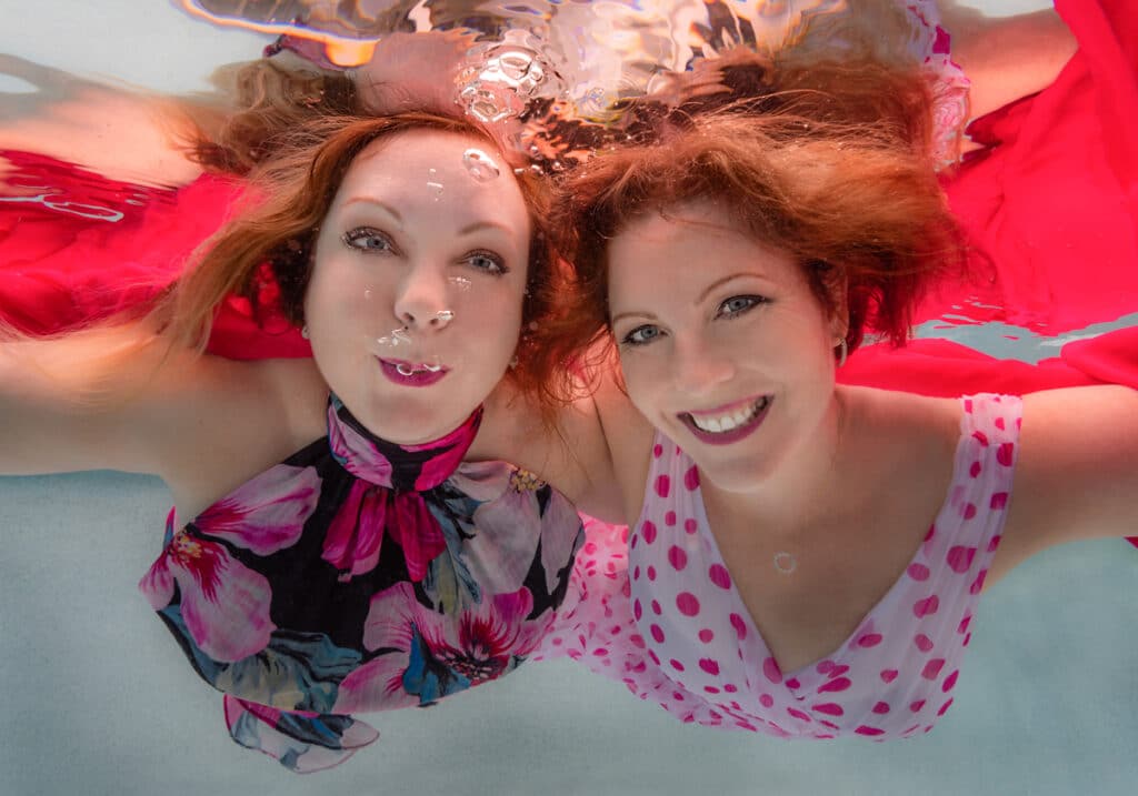 two women smiling and blowing bubbles underwater