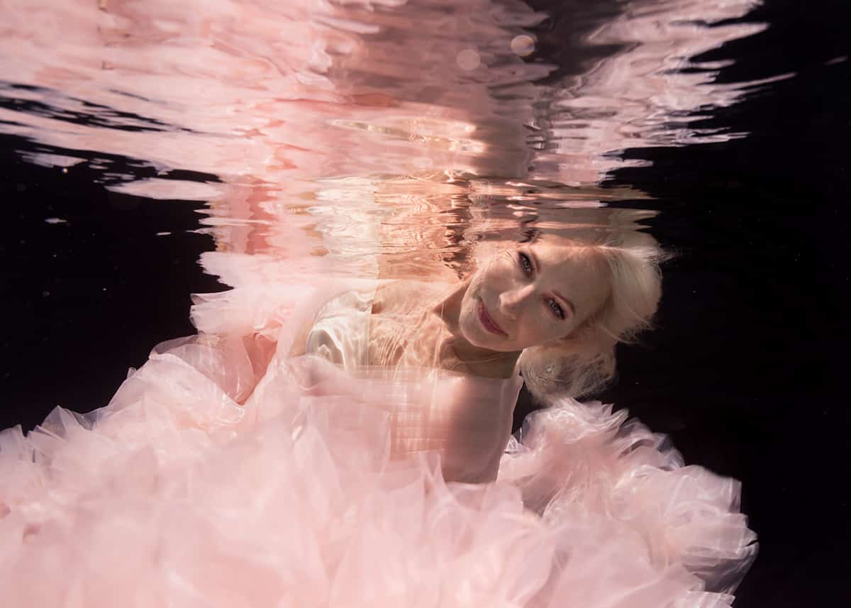 60+ beautiful blonde woman underwater wearing a voluminous pink gown