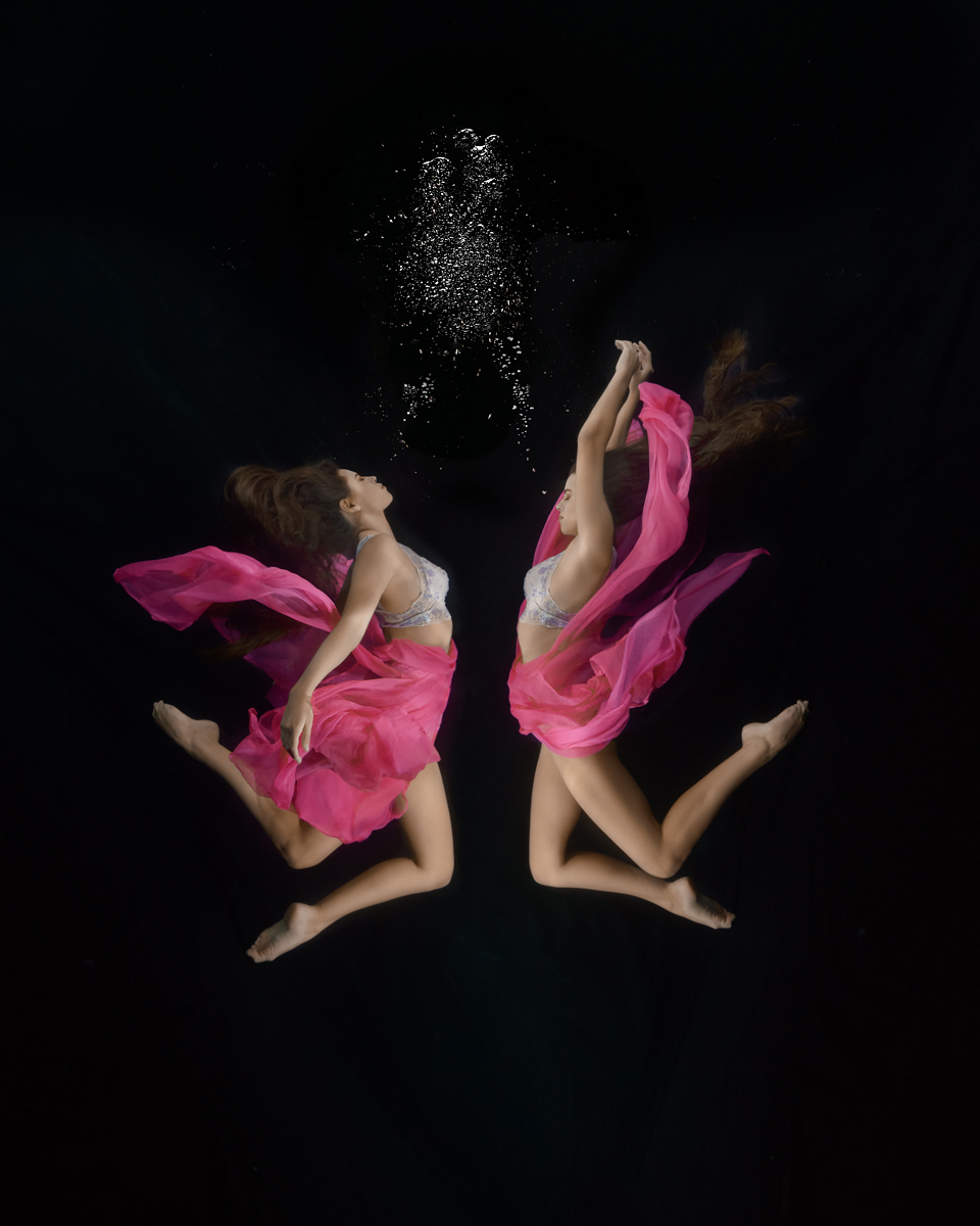 Artistic underwater portrait of a woman in two mirrored poses, blended into one surreal image with a black background, created in Noosa on the Sunshine Coast, Queensland.