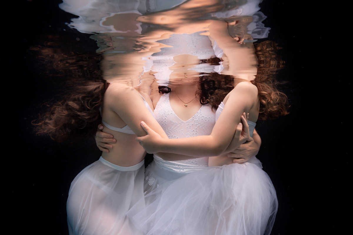 Underwater mother and daughter family photoshoot in Noosa, with professional makeup, wardrobe, and a luxurious editorial portrait experience. A quiet, dreamlike moment shared between a mother and her two daughters during an underwater family photoshoot. With professional makeup, flowing wardrobe, and the stillness of the water, the session becomes more than a portrait — it’s an experience of connection and memory-making.