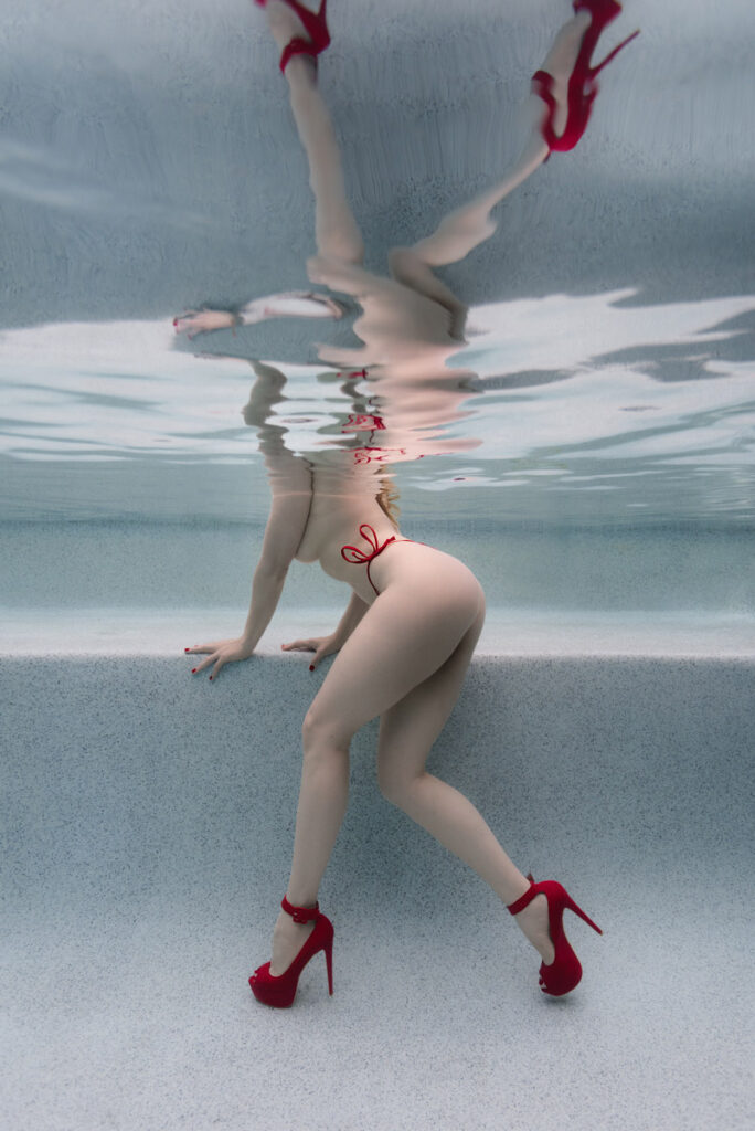 Underwater boudoir portrait with red high heels, celebrating female empowerment and sensual self-love in a luxury pool studio.